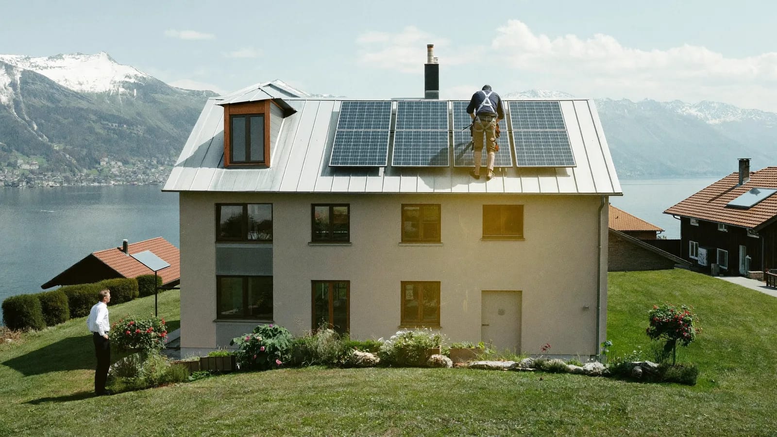 Des couvreurs posent des panneaux solaires sur une maison rénovée au-dessus d'un lac, Alpes en arrière-plan