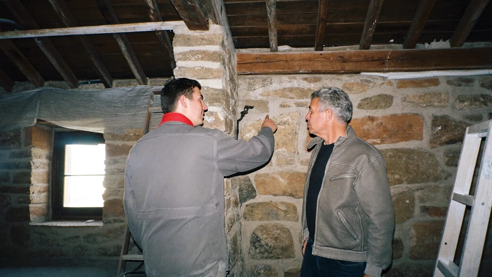 Un artisan montre une fissure dans un mur en pierre d'une ancienne maison en rénovation à son propriétaire